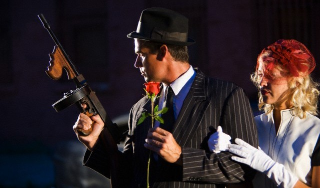 Gangster holding Tommy gun and rose with girlfriend clinging to arm
